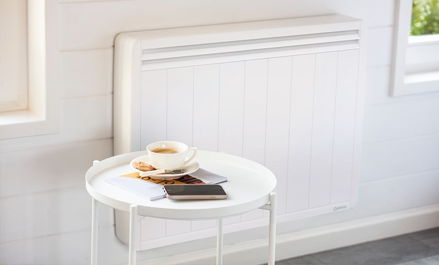 dettaglio di camera con pareti in legno riscaldamento elettrico a parete e un tavolino con caffè e quaderni davanti al termosifone